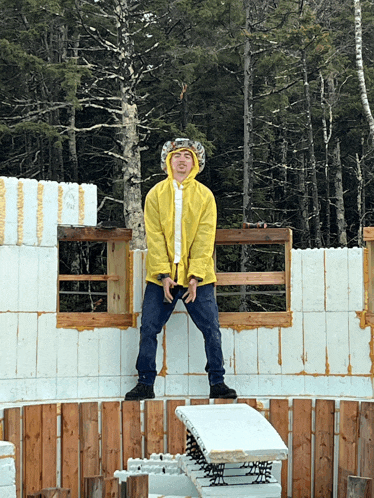 a man wearing a yellow raincoat and a hat stands on a wooden block
