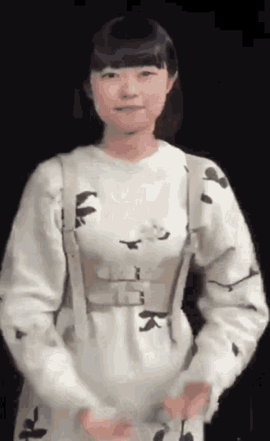 a woman wearing a white dress and a white belt is standing in front of a black background .