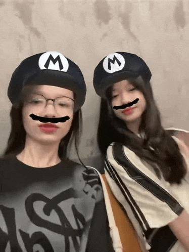 two girls wearing hats with the letter m on them and fake mustaches on their faces .