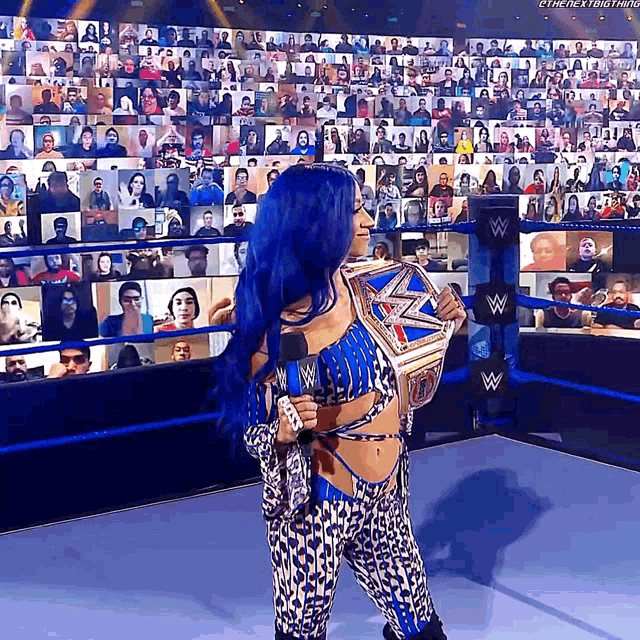 a woman with blue hair is holding a wrestling championship while standing in front of a crowd