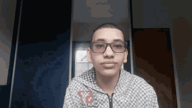 a young man wearing glasses and a checkered jacket with the number 12 on the front