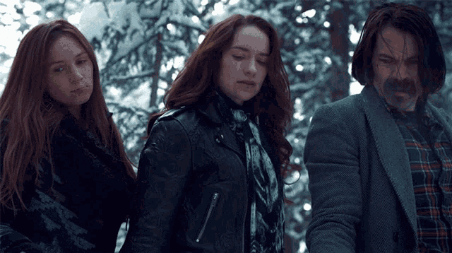 a man and two women are standing next to each other in a snowy forest