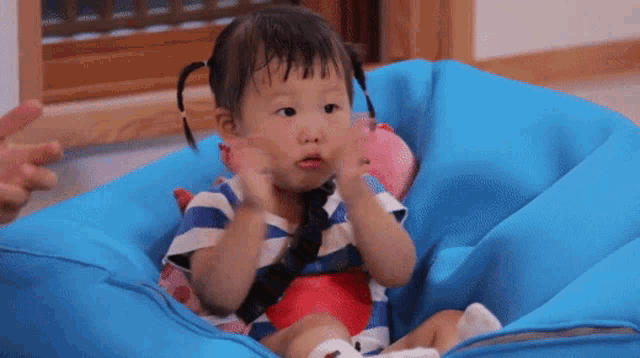 a little girl is sitting in a blue chair with her hands in the air .
