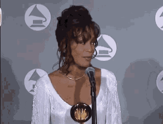 a woman in a white dress is standing in front of a microphone at a grammy awards press conference .