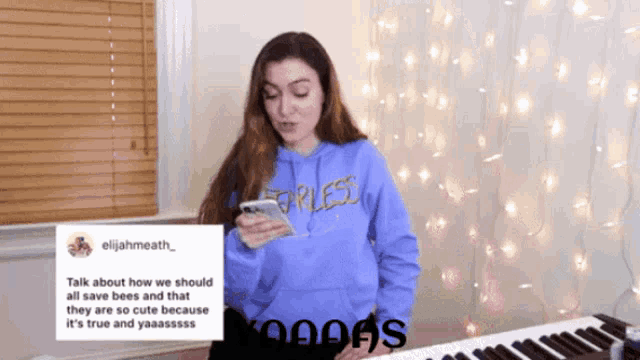 a girl wearing a blue sweatshirt that says fearless looks at her phone