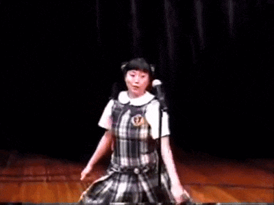 a girl in a plaid dress is dancing in front of a microphone