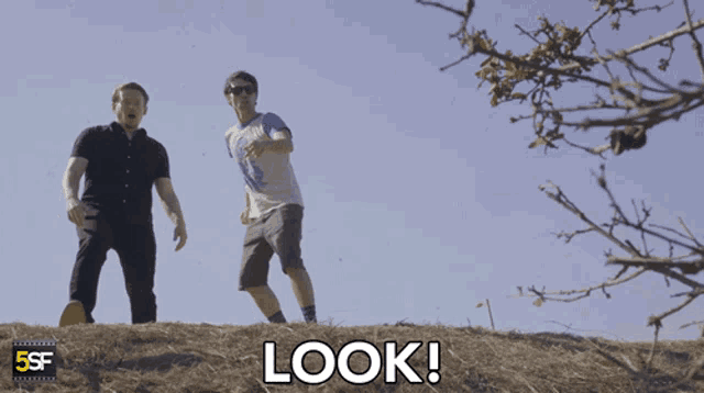 two men are standing on top of a hill and the word look is on the ground