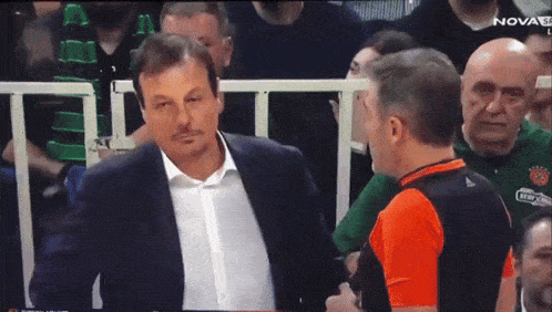 a man in a suit is talking to a referee in an orange shirt that says nova on it