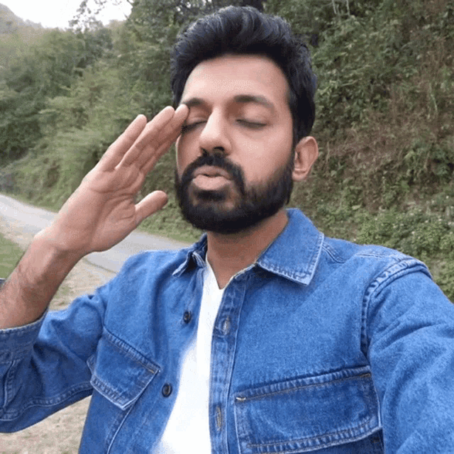 a man with a beard wearing a denim shirt salutes