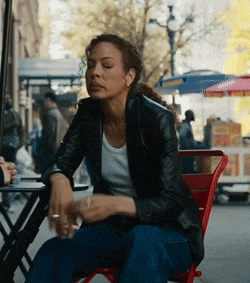 a woman in a black jacket sits at a table with her eyes closed