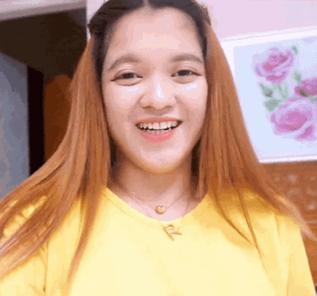 a woman wearing a yellow shirt and necklace with the letter r on it
