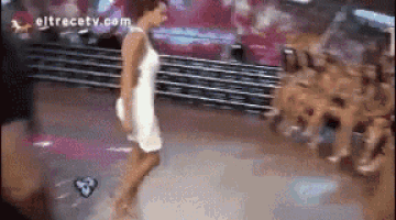 a woman in a white dress is dancing in front of a crowd with eltrecetv.com written on the bottom right