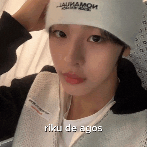 a woman wearing a white hat and a black jacket with the words riku de agos on the bottom .