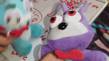 a purple stuffed animal is being held by a person in front of a white board with the word love written on it