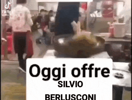 a group of people are standing around a table with a sign that says oggi offre silvio berlusconi .