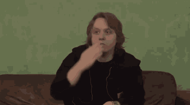 a young man is sitting on a couch and making a funny face with his hands .