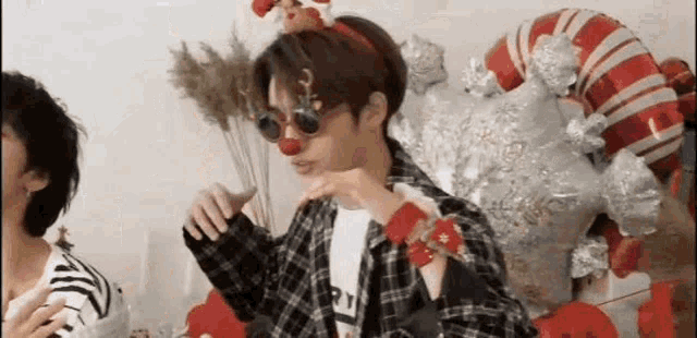 a young man wearing sunglasses and a santa hat is standing in front of a christmas tree .