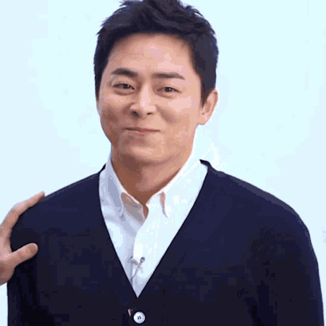 a man wearing a black cardigan and a white shirt has a hand on his shoulder