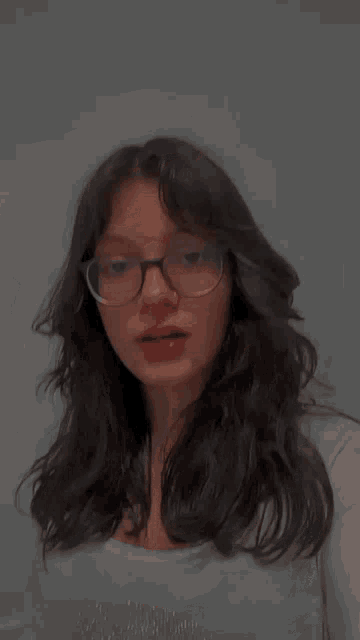 a woman wearing glasses and a nose ring holds her hand to her forehead