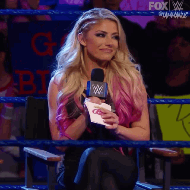 a woman in a wrestling ring is holding a piece of paper and a microphone
