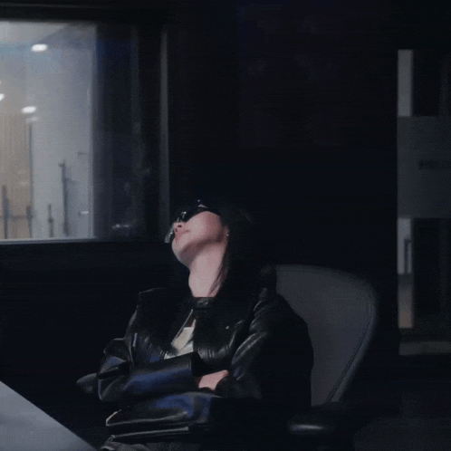 a woman wearing sunglasses sits in a dark room