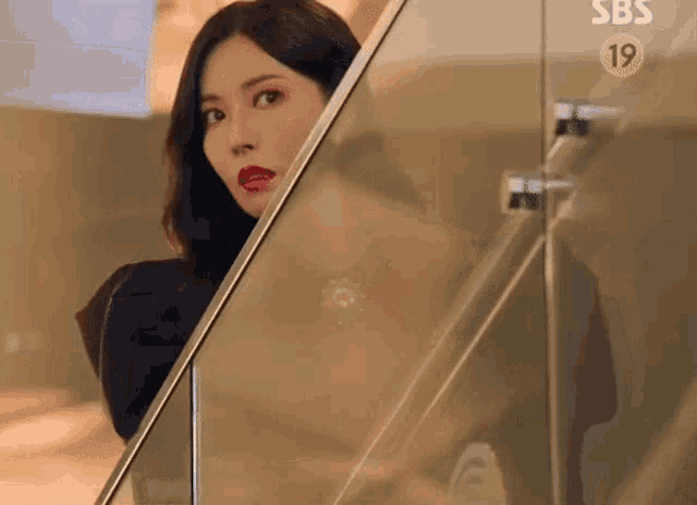 a woman with red lipstick is peeking out from behind a glass door .