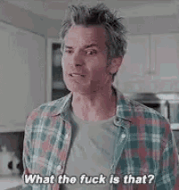 a man in a plaid shirt is standing in a kitchen talking to someone .