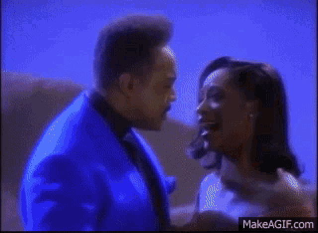 a man in a blue suit is kissing a woman in a red dress