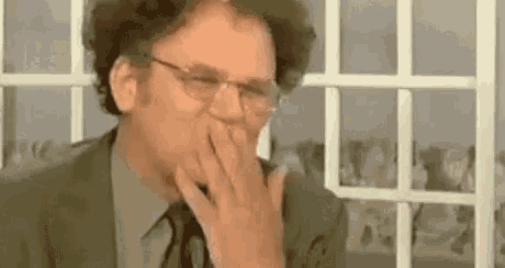 a man wearing glasses is covering his mouth with his hand .