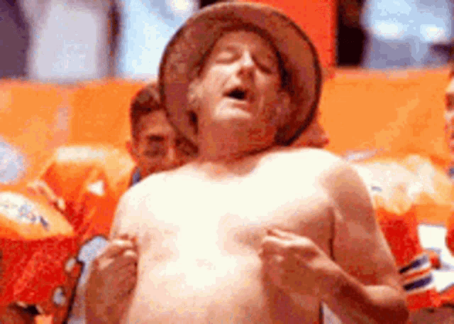 a shirtless man wearing a cowboy hat is standing in front of a crowd .