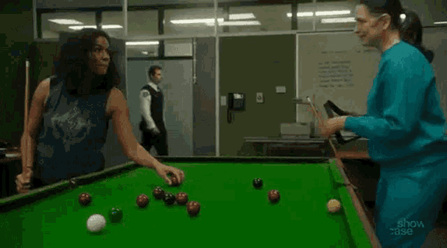 two women are playing pool on a pool table in a jail cell .