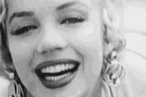 a black and white photo of a woman smiling and wearing earrings .
