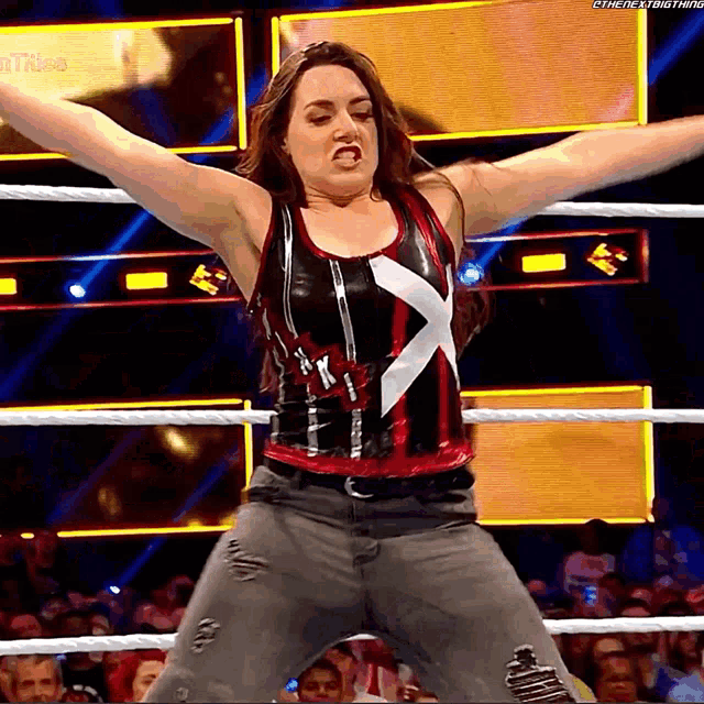 a woman is standing in a wrestling ring with her arms outstretched in front of a screen that says " the next thing "