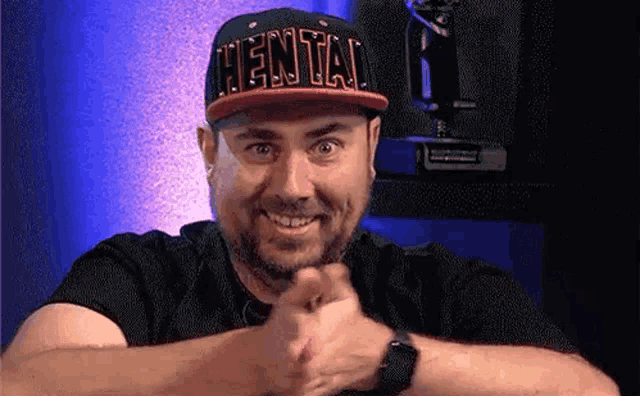 a man wearing a hat with the word hentai on it is smiling and making a funny face .