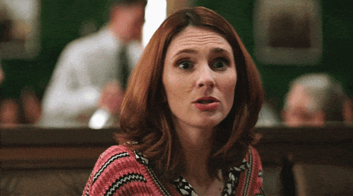 a woman with red hair and a pink sweater looks surprised