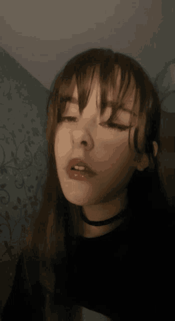 a close up of a woman 's face with her eyes closed and a choker around her neck