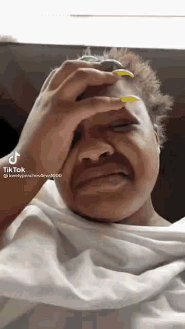 a woman with yellow nails is crying and covering her face .