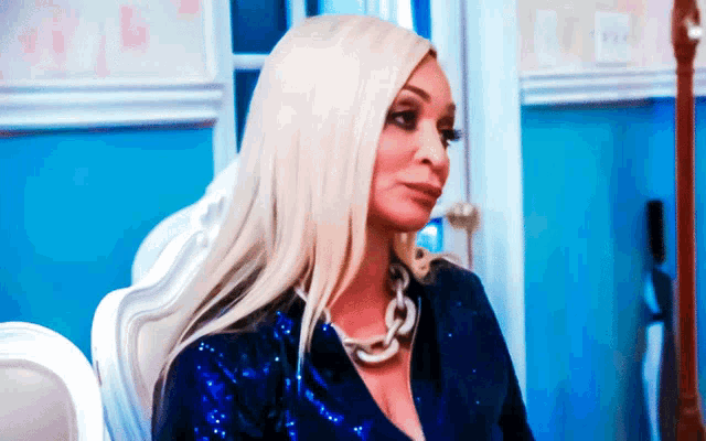 a woman wearing a blue sequined jacket and a chain around her neck