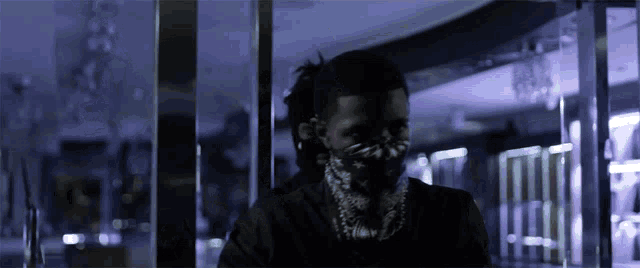 a man with a bandana on his face stands in front of a glass wall