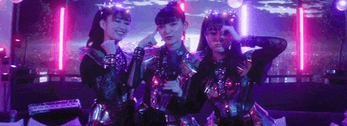 three girls in futuristic costumes are standing next to each other in a dark room .