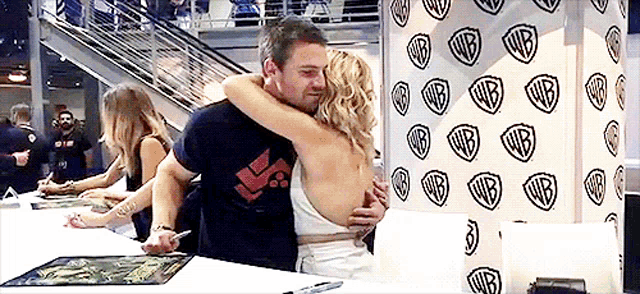 a man and a woman hugging in front of a wall with wb logos