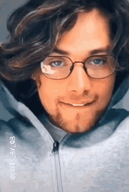 a man wearing glasses and a hooded jacket is smiling