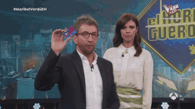 a man in a suit stands next to a woman in a white shirt in front of a sign for el hormiguero