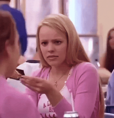 a woman in a pink sweater is sitting at a table with a piece of cake in her hand .