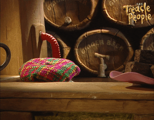 a colorful knitted hat sits on a wooden table in front of wooden barrels that say ginger beer