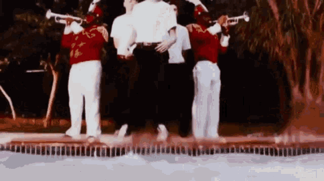 a group of people are standing next to a pool playing trumpets .