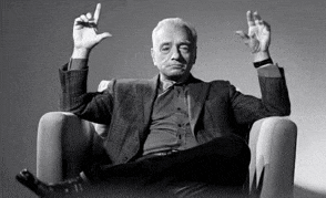 a man in a suit is sitting in a chair with his legs crossed and his hands up in the air .