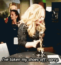 a woman is sitting at a table holding an oscar statue and saying i 've taken my shoes off sorry