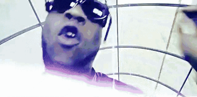a man wearing sunglasses and a pink shirt is standing in a room with a white background .
