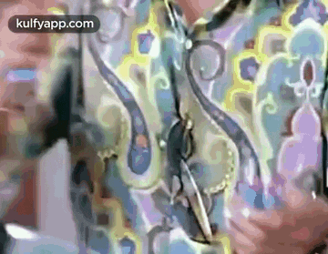 a man in a colorful shirt is holding a pair of scissors in his hand .